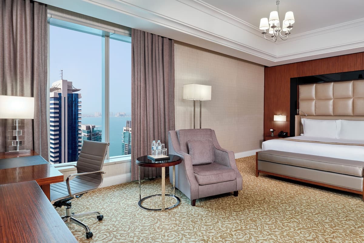 Une chambre d’hôtel avec un grand lit, un bureau, une chaise, une petite table et une vue sur le paysage urbain.