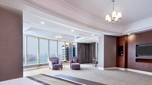 Quarto de hotel com uma cama grande, duas poltronas, uma escrivaninha, televisão e vista para a cidade.