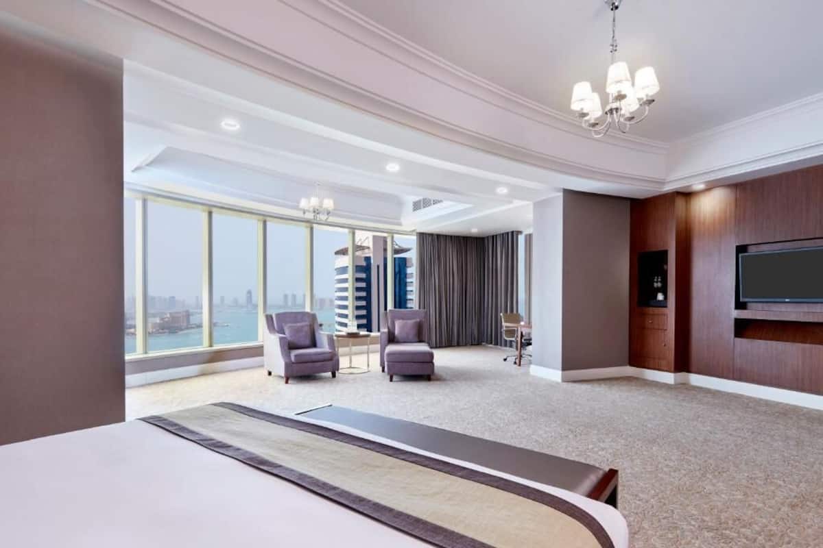 Une chambre d’hôtel avec un grand lit, deux fauteuils, un bureau, une télévision et une vue sur la ville.