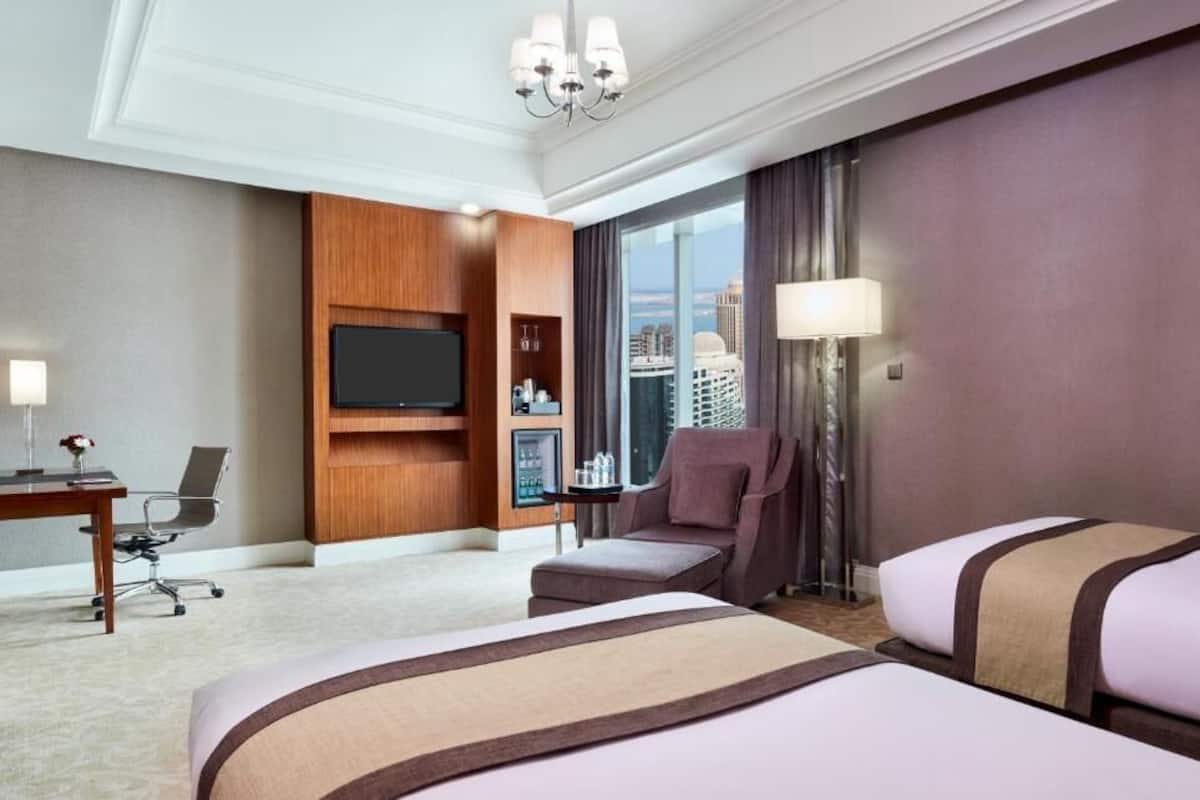 Une chambre d’hôtel avec deux lits, une télévision, un bureau avec une chaise, une lampe et une vue sur la ville.