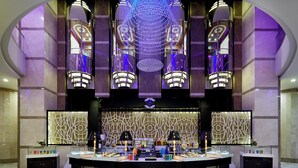 Um hall luxuoso com um bar circular central, iluminação decorativa e um painel de parede estampado.