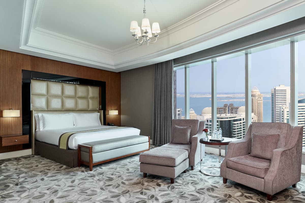 Une chambre d’hôtel avec un grand lit, une chaise longue, une petite table et une vue sur le paysage urbain.