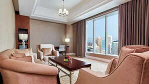 Quarto de hotel com uma janela grande, um conjunto de sofás, uma mesa de jantar e um abajur.