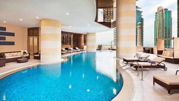 Piscina interior moderna com espreguiçadeiras e vista para edifícios altos.