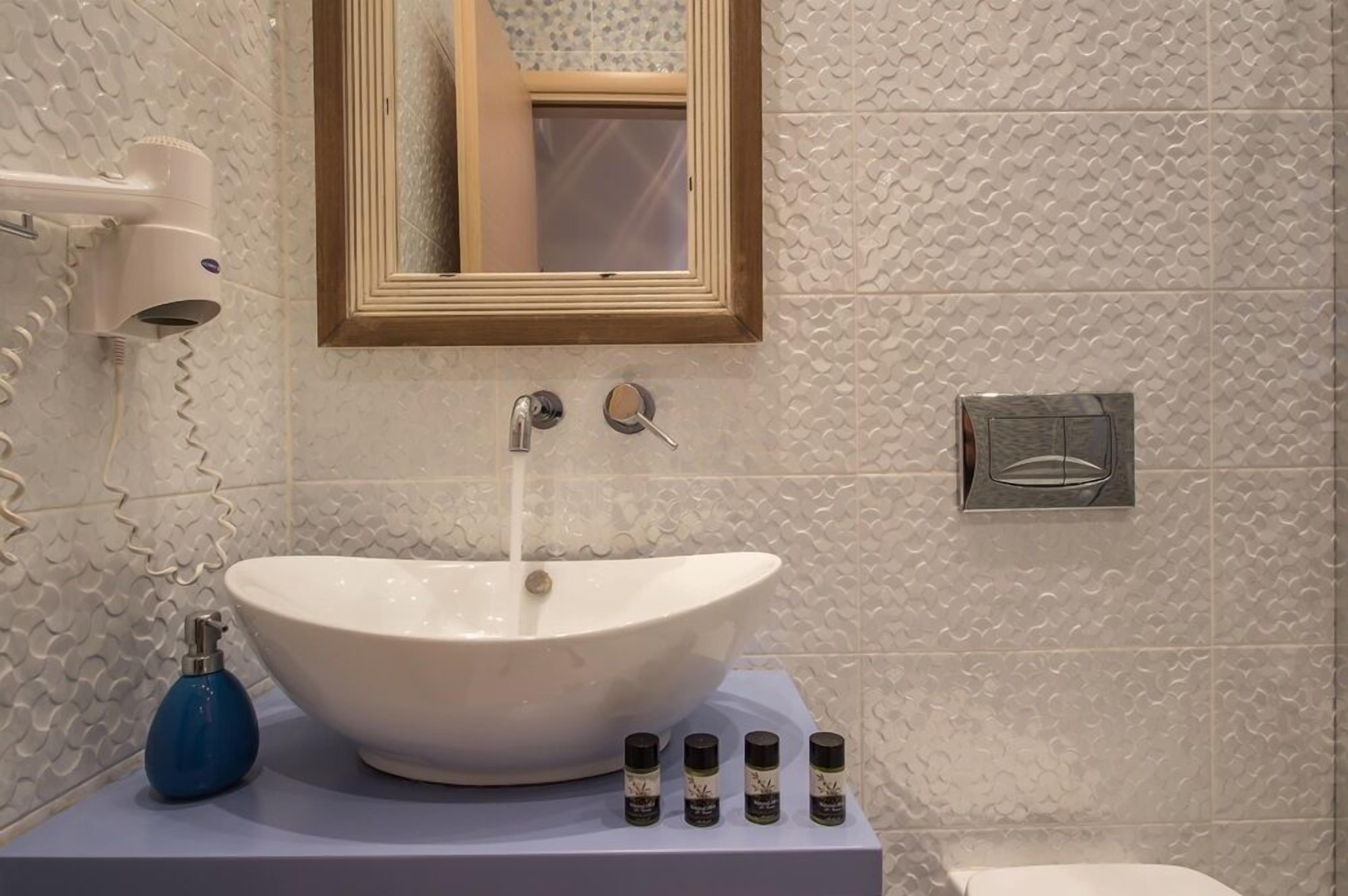 A bathroom with a white sink, a hairdryer, and four small bottles on the counter.
