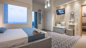 A modern bedroom with a large bed, a TV, and a view of the sea. - Aphrodite Studios (Astypalaia)
