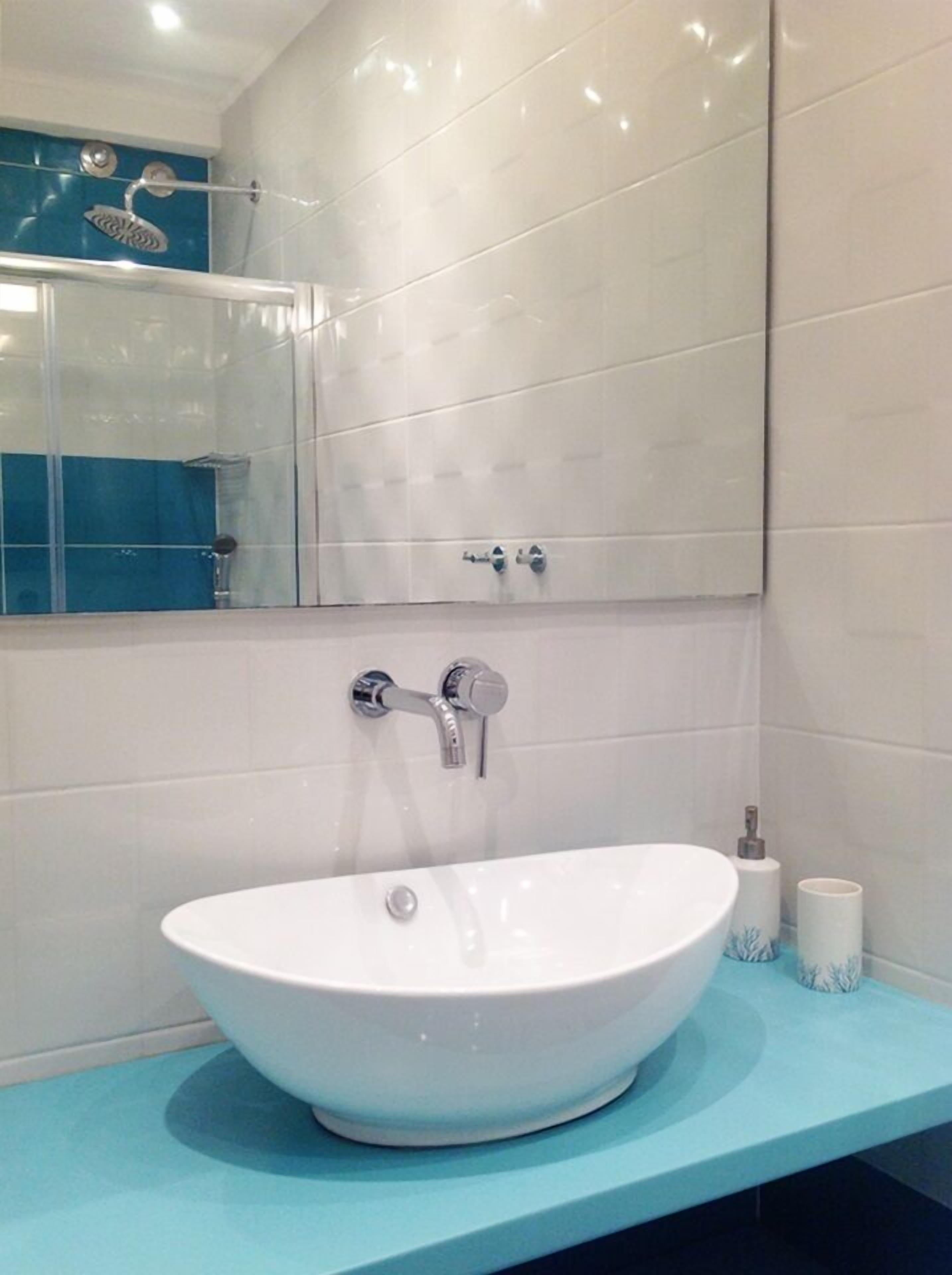 Une salle de bain avec un lavabo blanc, un miroir et une cabine de douche.