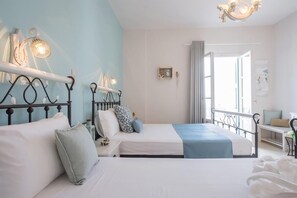A bedroom with two beds, a nightstand, a desk, and a window with curtains. - Aphrodite Studios (Astypalaia)