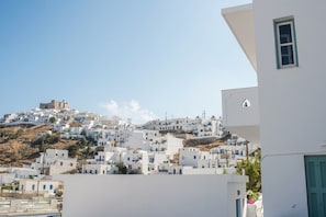 A coastal village with white buildings on a hillside, a prominent ancient structure, and a modern building with a window and door. - Aphrodite Studios (Astypalaia)