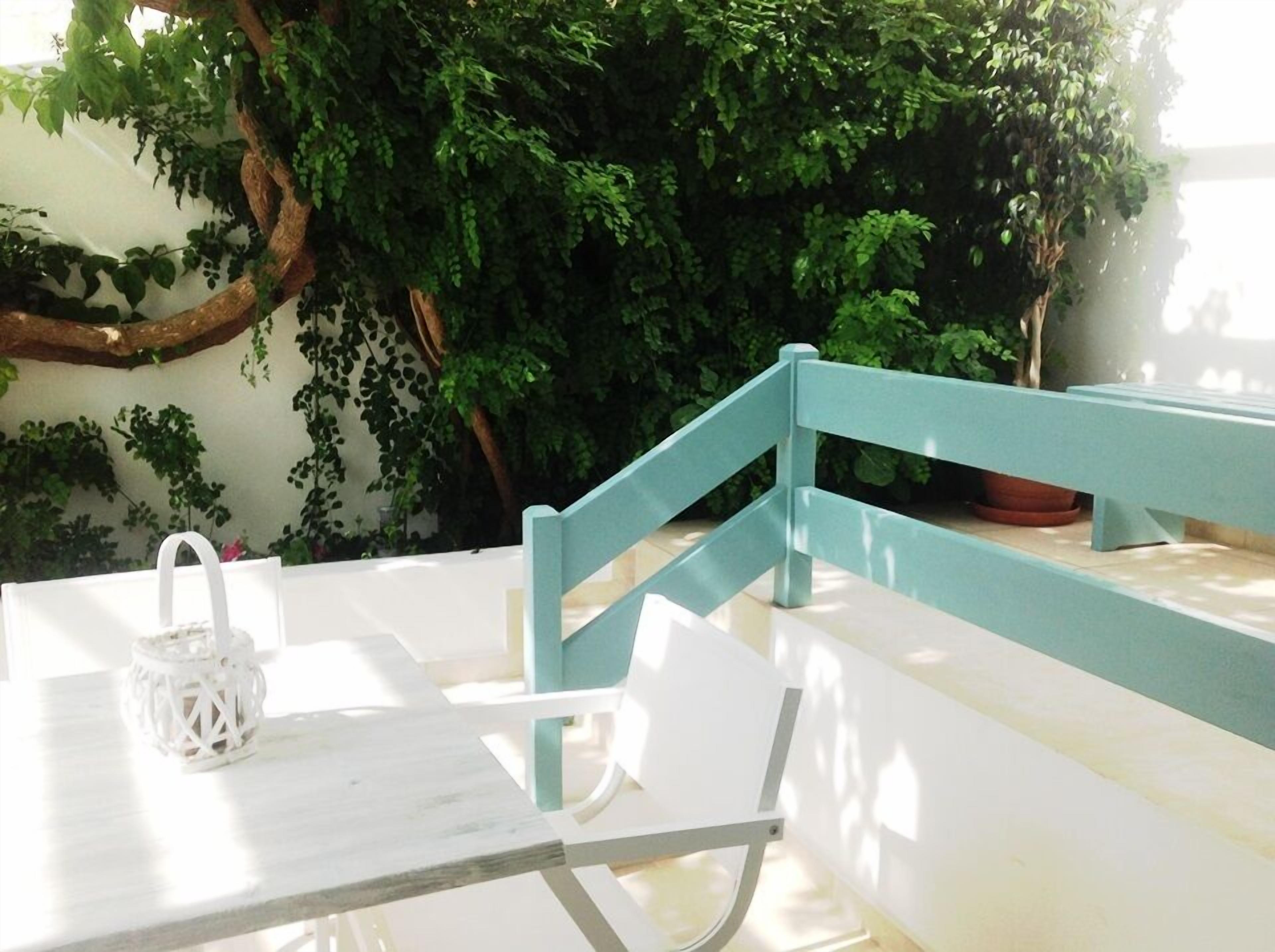 Una mesa blanca con un farol blanco y un banco azul en un jardín con follaje verde.