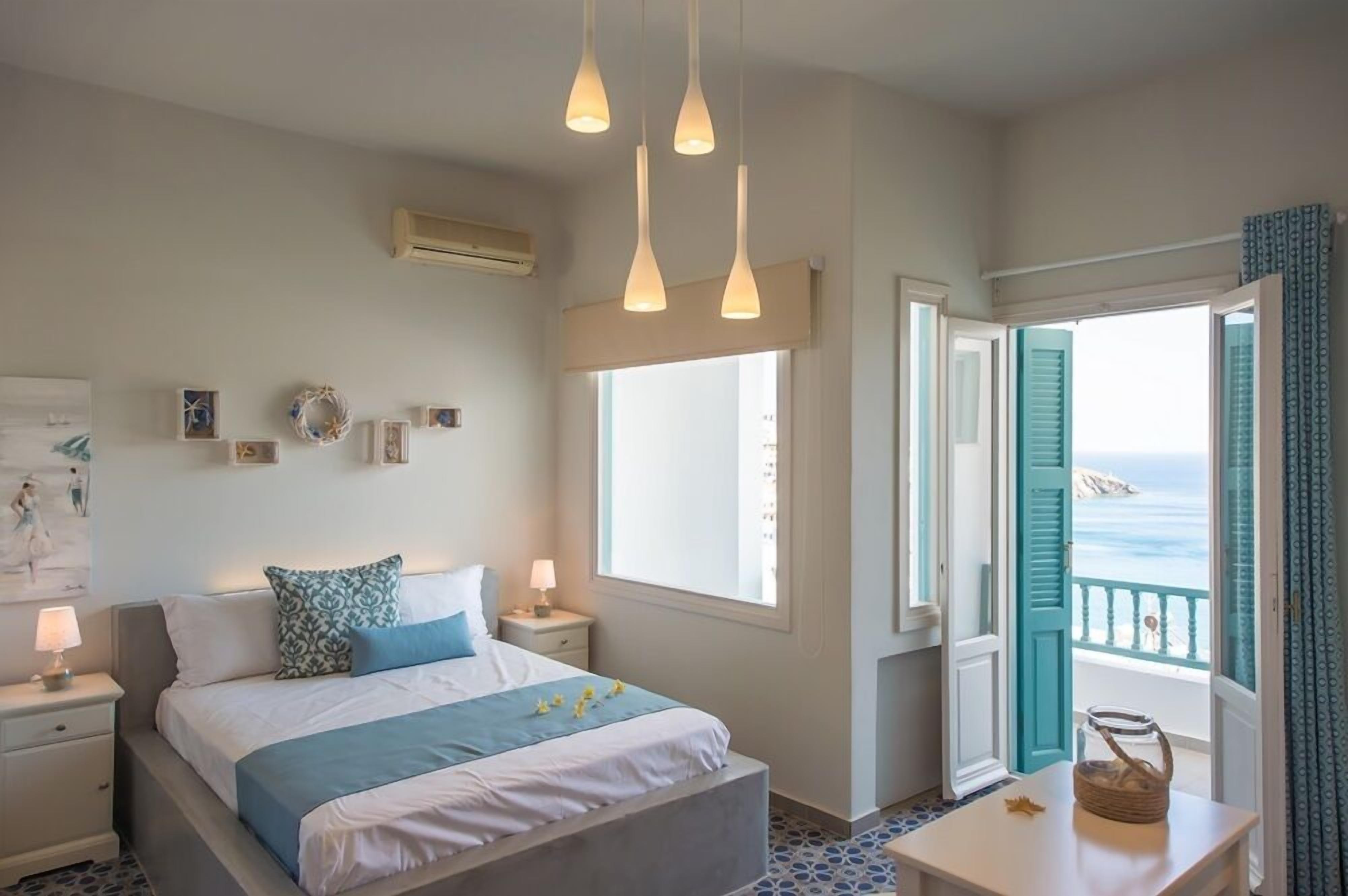 Ein Schlafzimmer mit Bett, Nachttischen, einem Fenster mit Meerblick und einem Balkon mit Geländer.