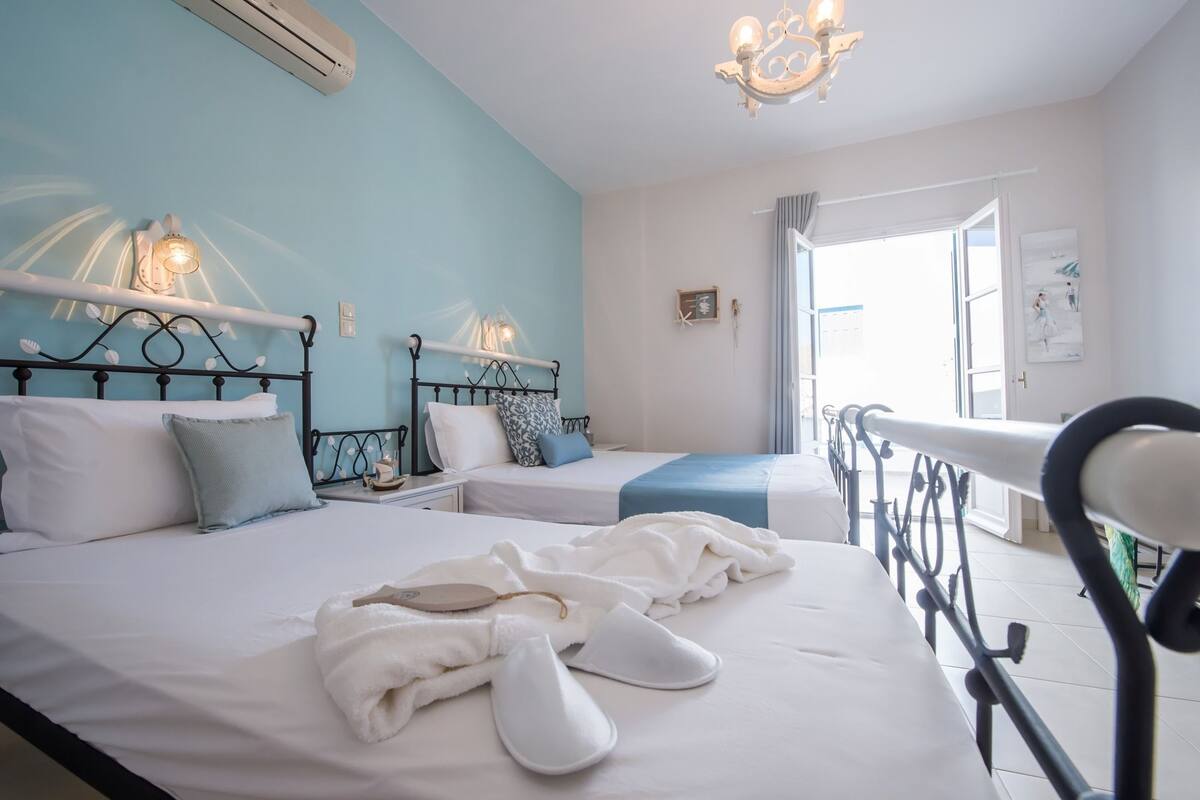 A hotel room with two beds, a chandelier, an air conditioner, and a view of the outside.