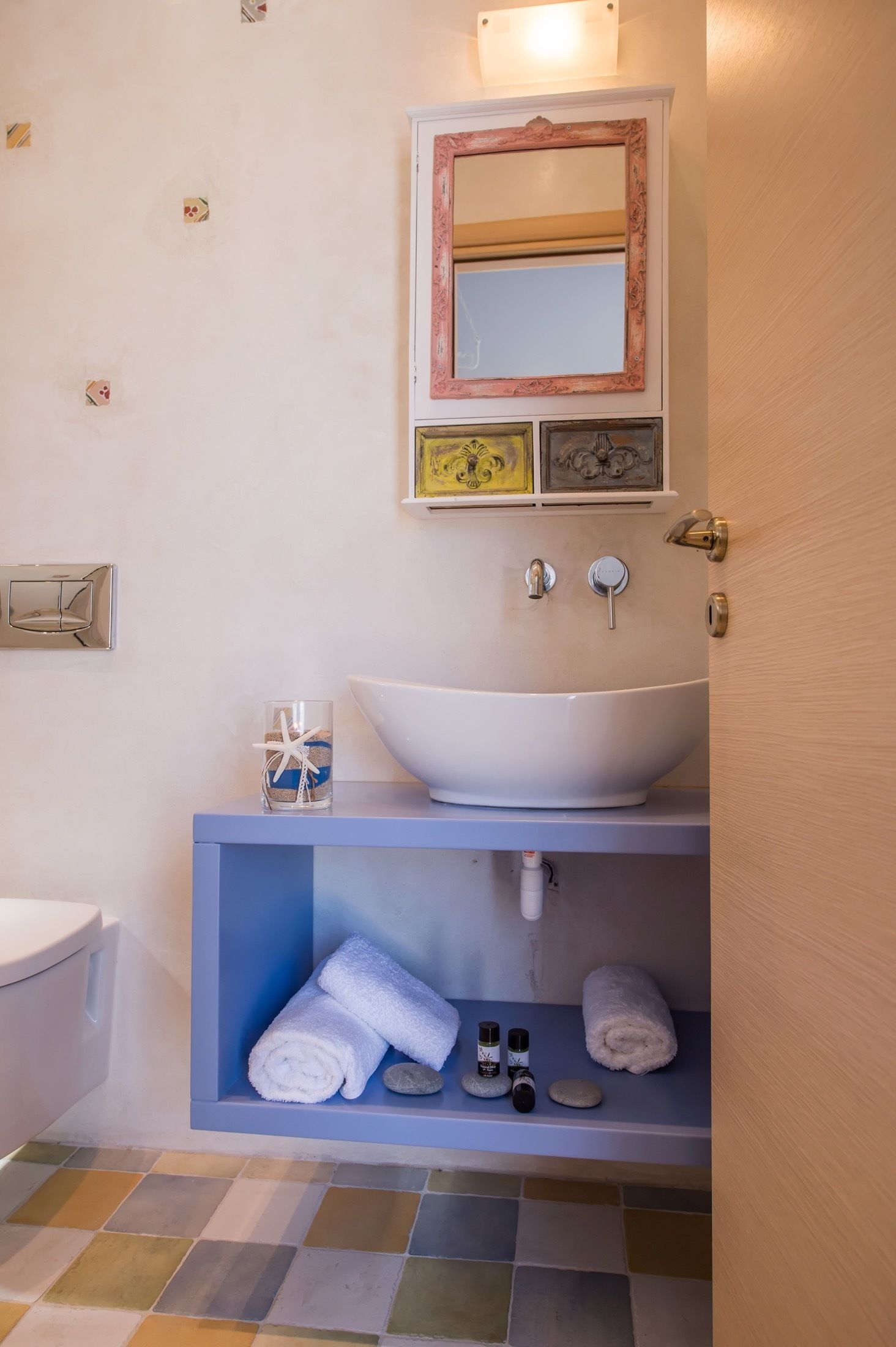 A bathroom with a white sink, a blue vanity, a mirror with a decorative frame, and a tiled floor.