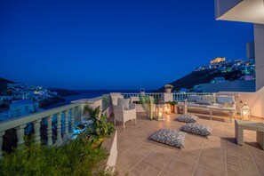 Une terrasse avec des sièges extérieurs, une vue sur la mer et une colline parsemée de bâtiments.