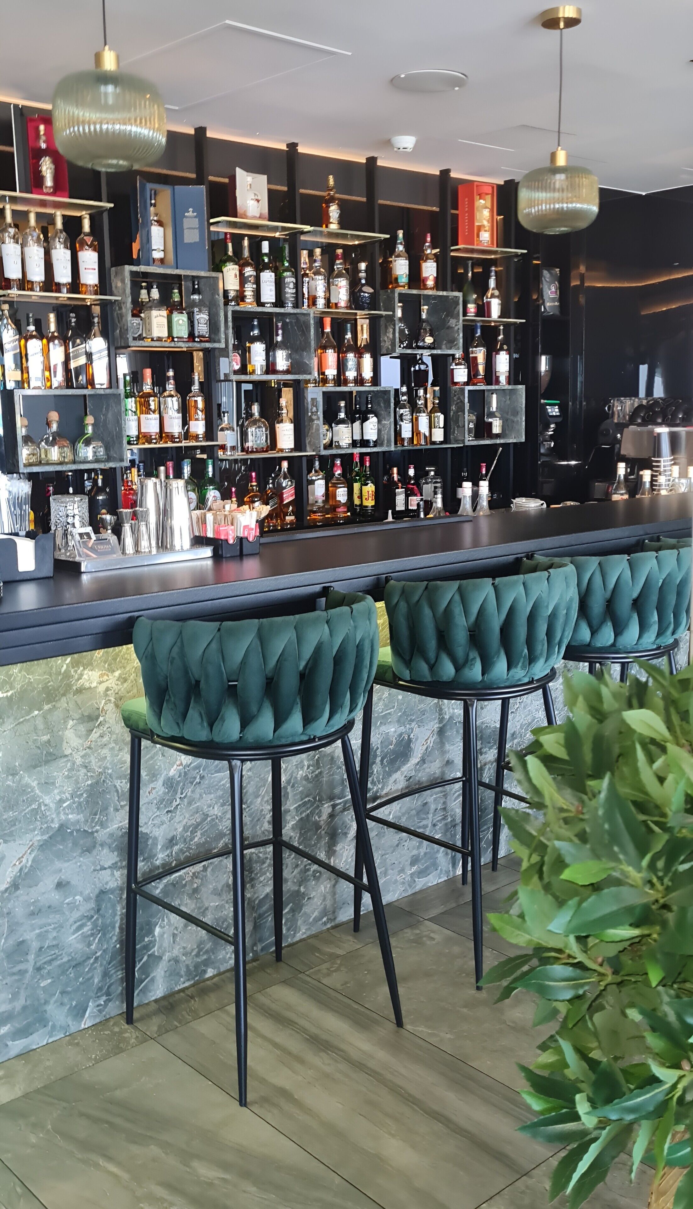 Un espace bar avec de nombreuses bouteilles d’alcool, un comptoir et des tabourets de bar recouverts d’un tissu vert.
