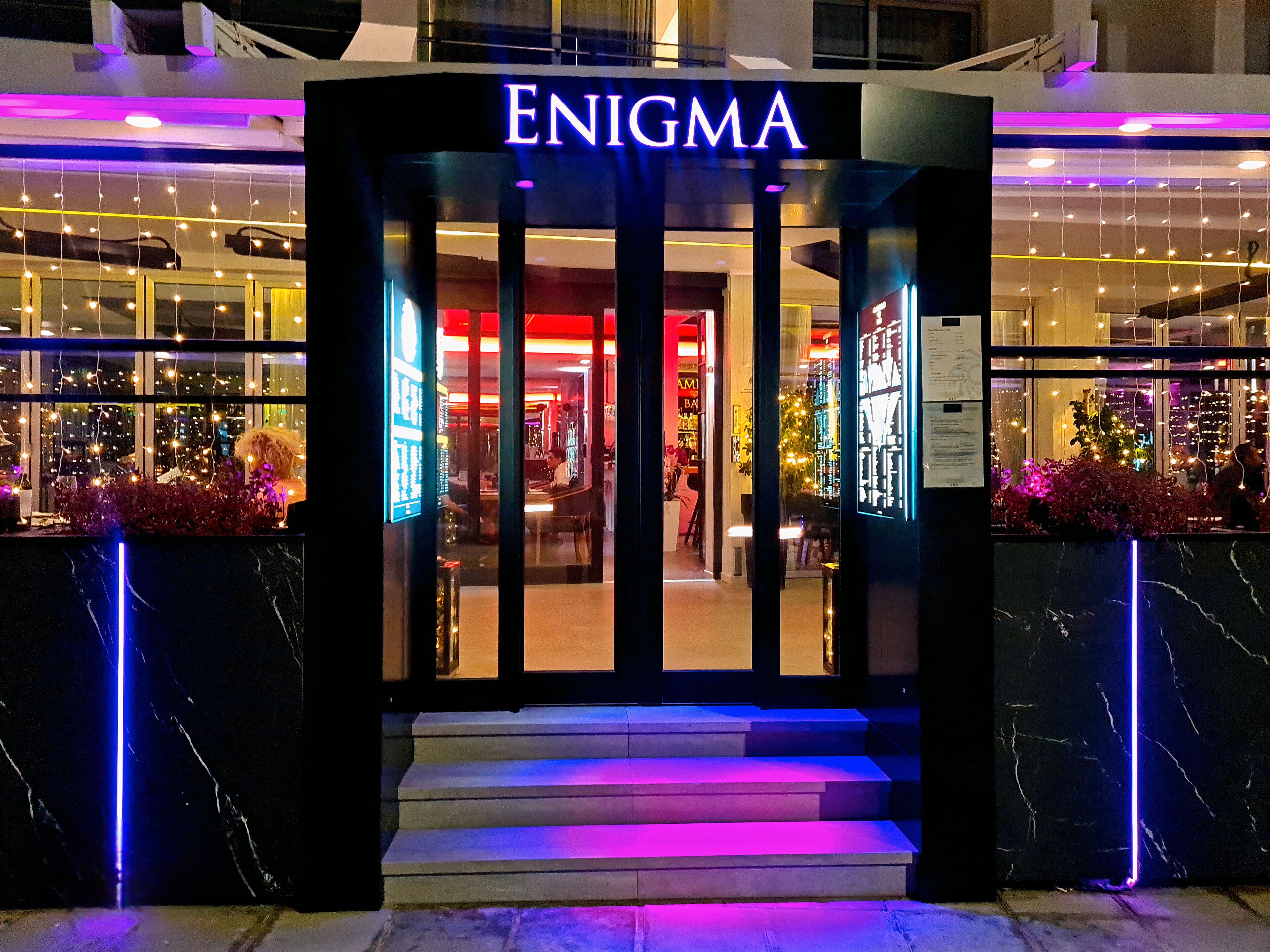 Der Eingang zu ENIGMA mit beleuchteter Beschilderung und Stufen, die zum Eingang führen.