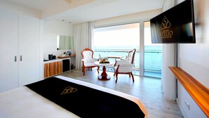 Une chambre d’hôtel moderne équipée d’un lit, d’une télévision, d’un balcon avec vue sur la mer et d’un coin repas avec des chaises et une table.