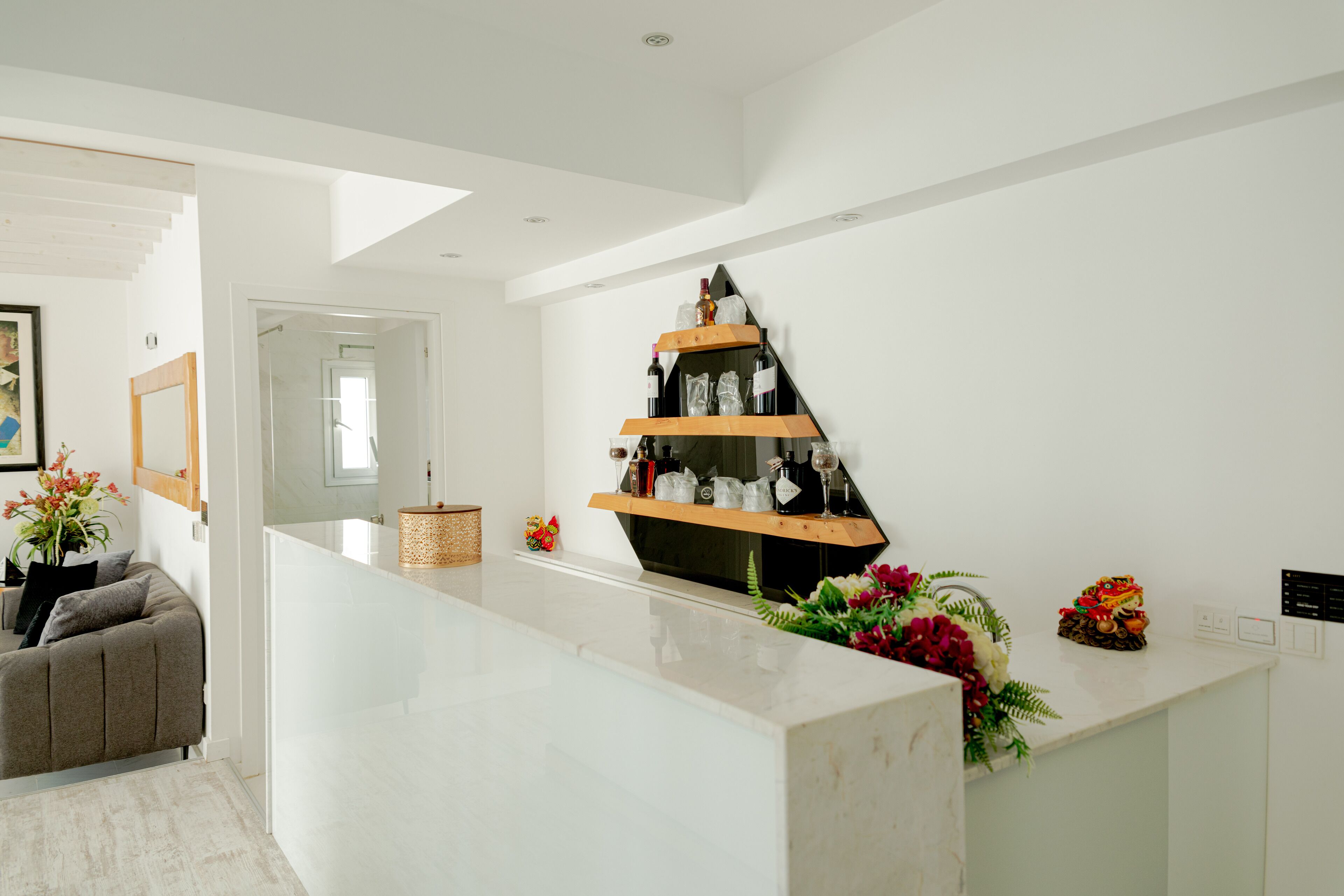 A modern reception area with a white marble counter, a wooden shelf with bottles, and a floral arrangement.