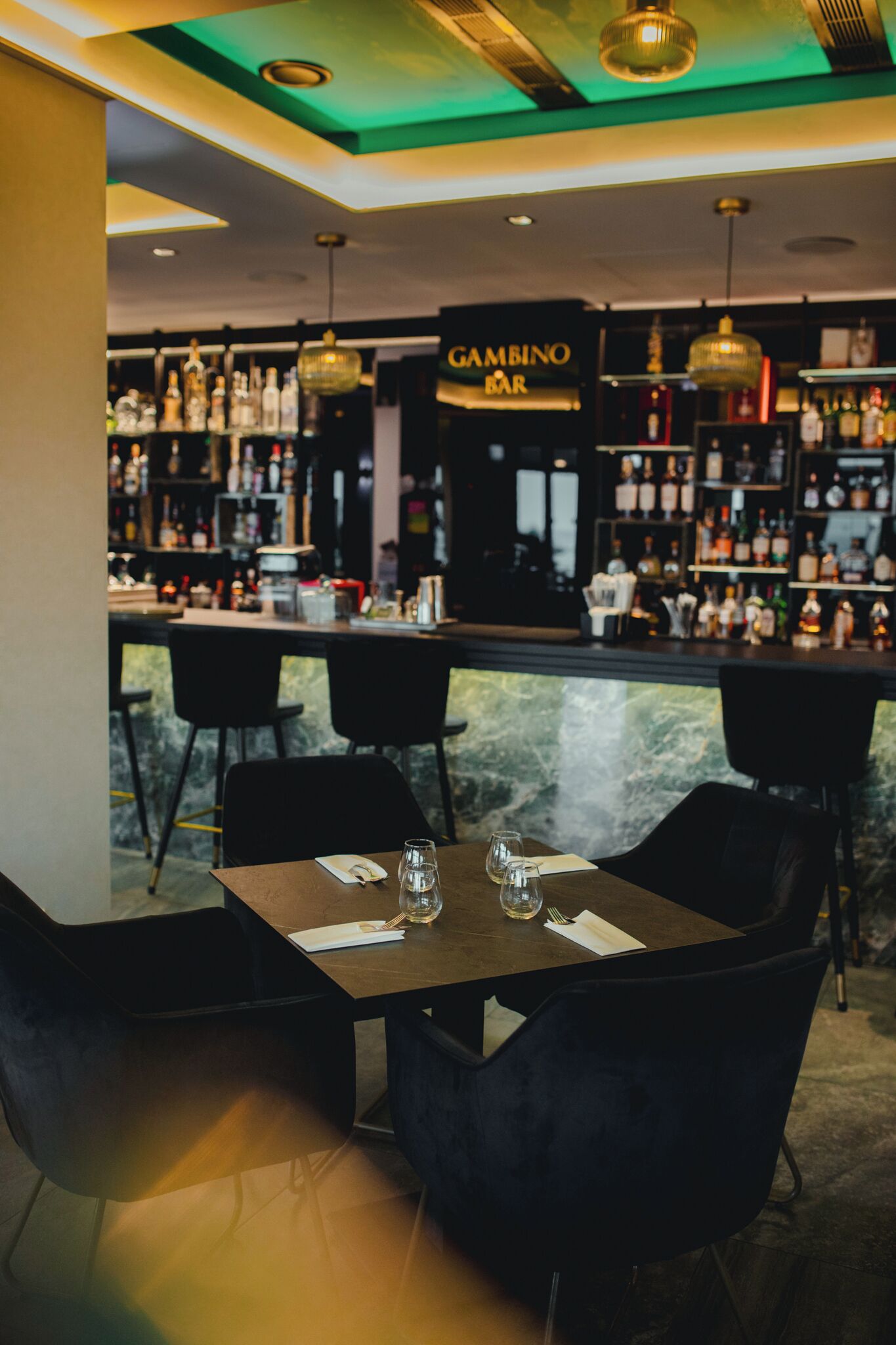 A bar area with a marble counter, black chairs, and a 'GAMBINO BAR' sign.