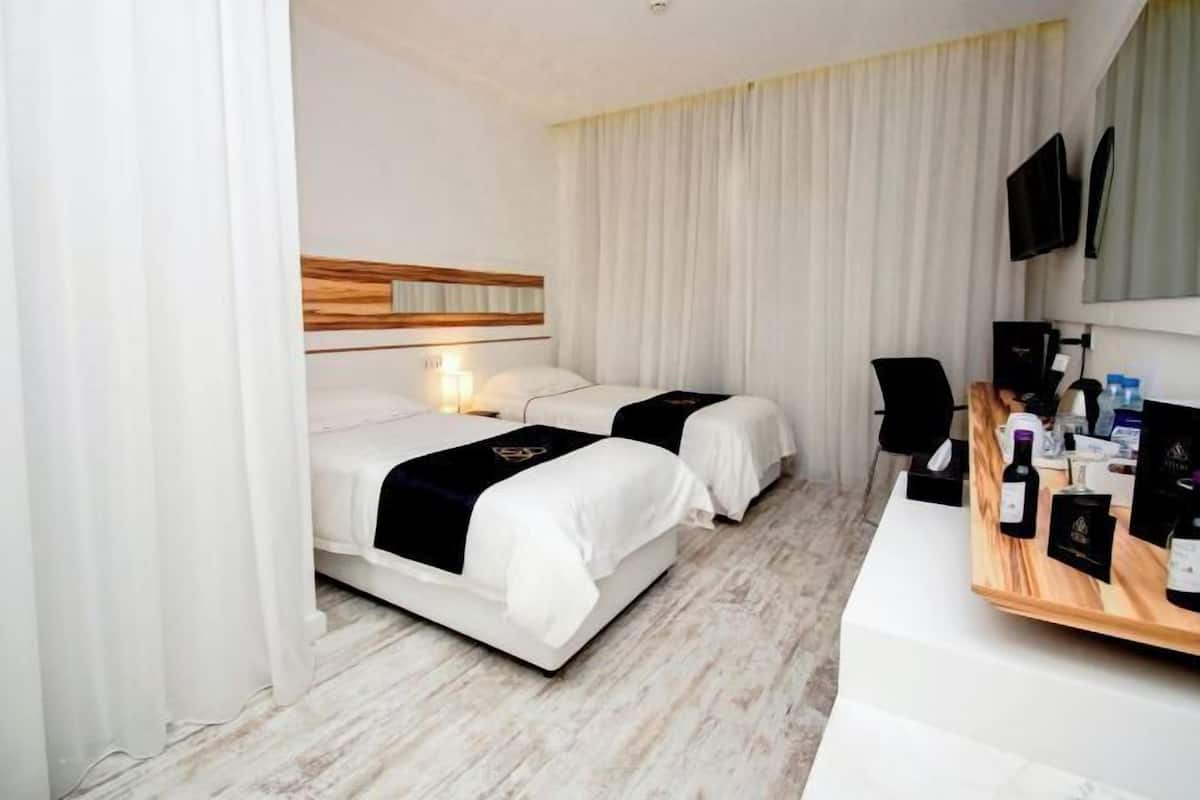 Une chambre d’hôtel avec deux lits, une tête de lit en bois, un bureau avec un ordinateur et une télévision.