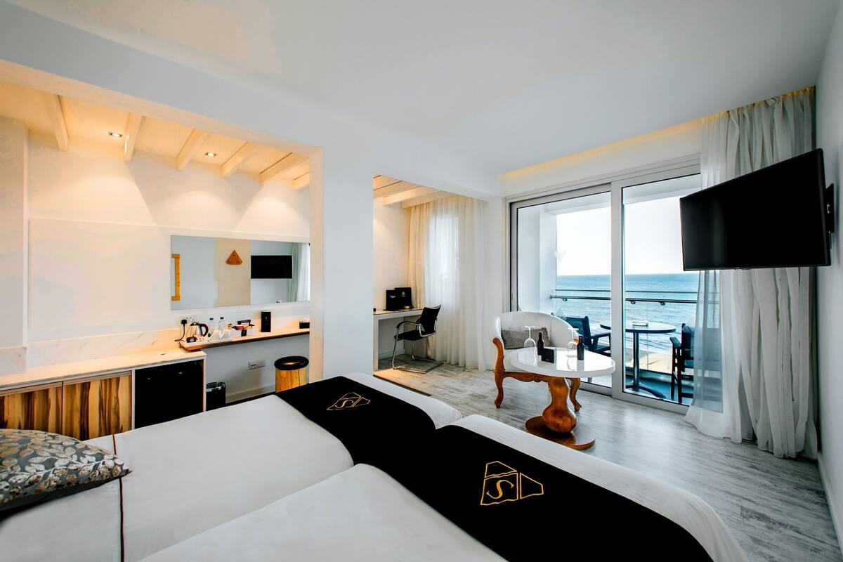 Une chambre d’hôtel moderne dotée d’un grand lit, d’un bureau, d’une chaise, d’une télévision et d’un balcon offrant une vue sur la mer.