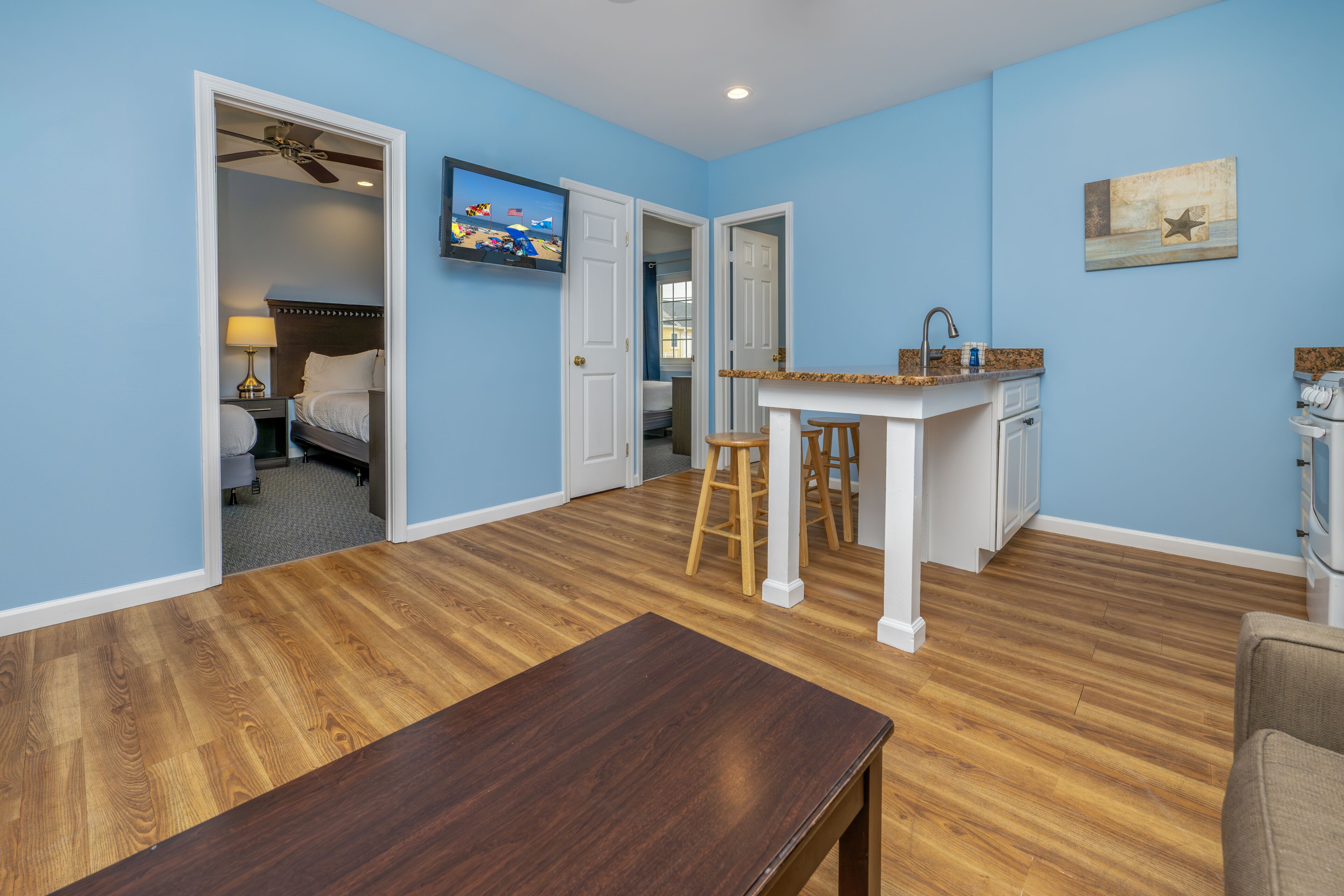 A room with a wooden floor, a bed, a desk, and a kitchenette.