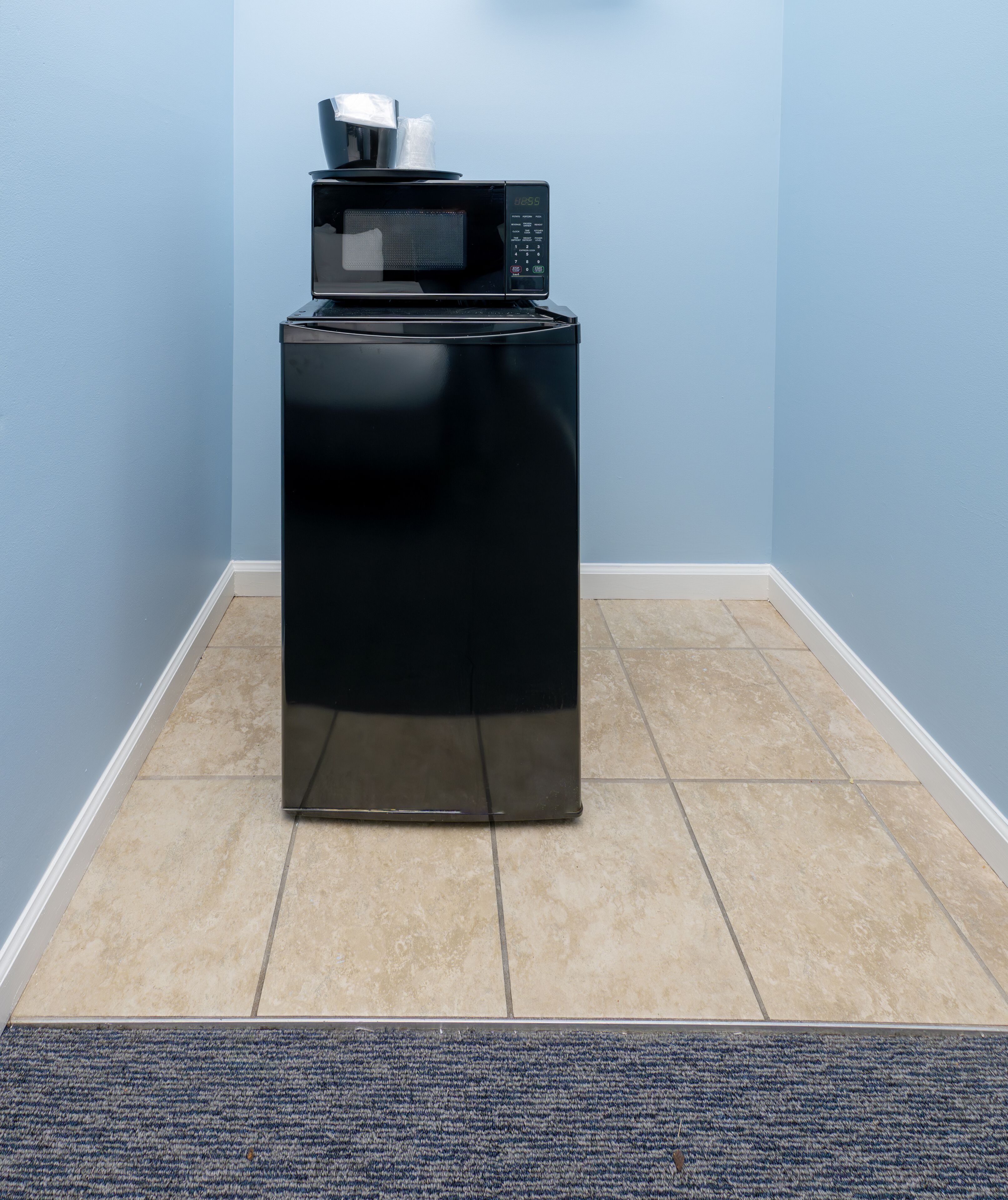 A compact black appliance with a digital display, possibly a microwave, on a tiled floor in a corner with blue walls.