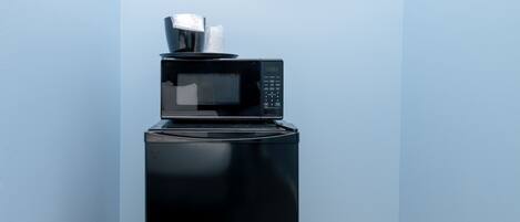 A compact black appliance with a digital display, possibly a microwave, on a tiled floor in a corner with blue walls.