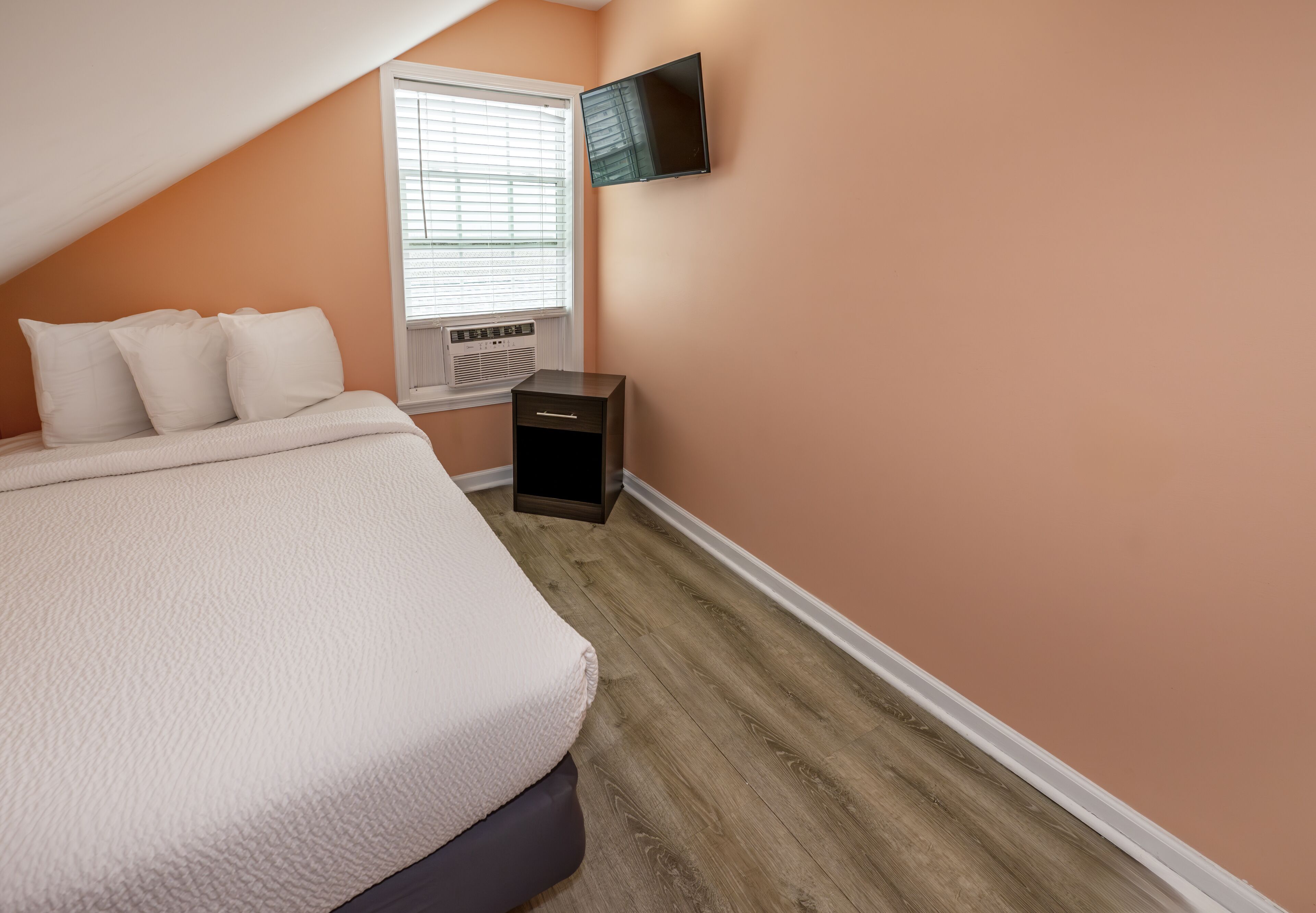 A bedroom with a bed, a nightstand, a TV, and a window with blinds.