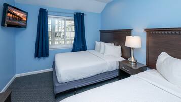 A hotel room with two beds, a TV mounted on the wall, a window with curtains, and a nightstand with a lamp.