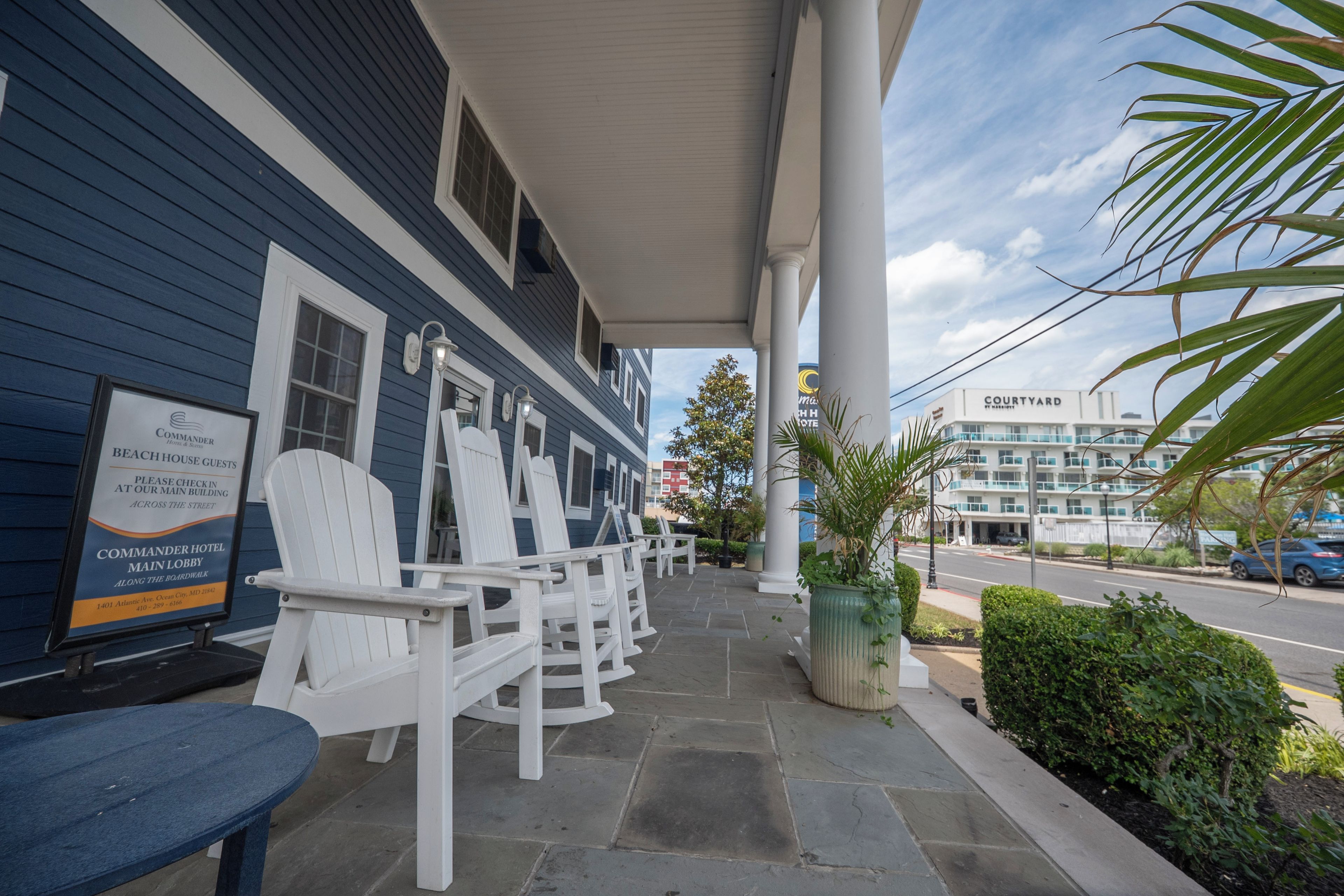 A hotel with a covered outdoor seating area, white chairs, and a sign for the Commander Hotel Main Lobby.