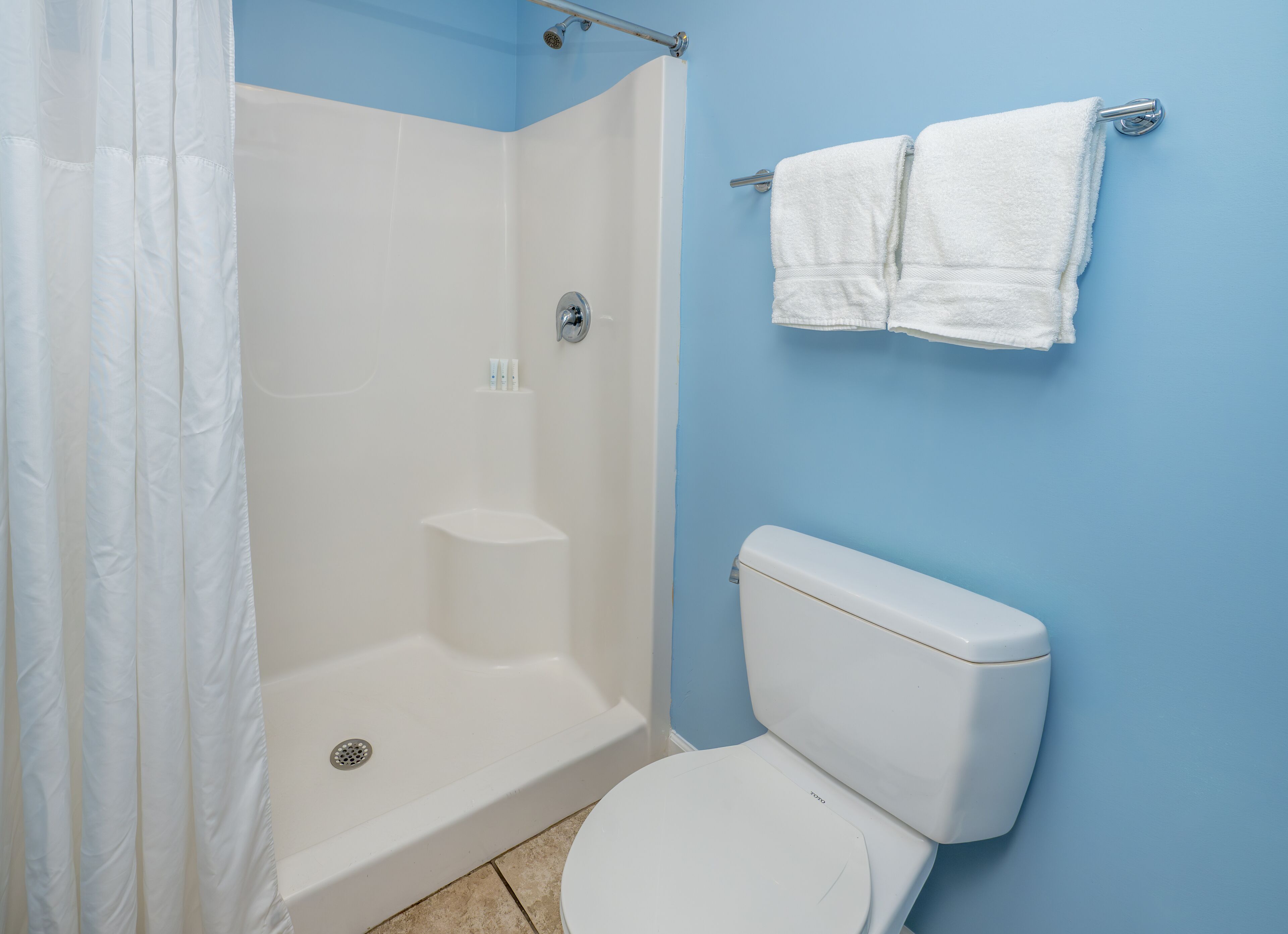Een badkamer met een douche, toilet en twee handdoeken aan een rek.