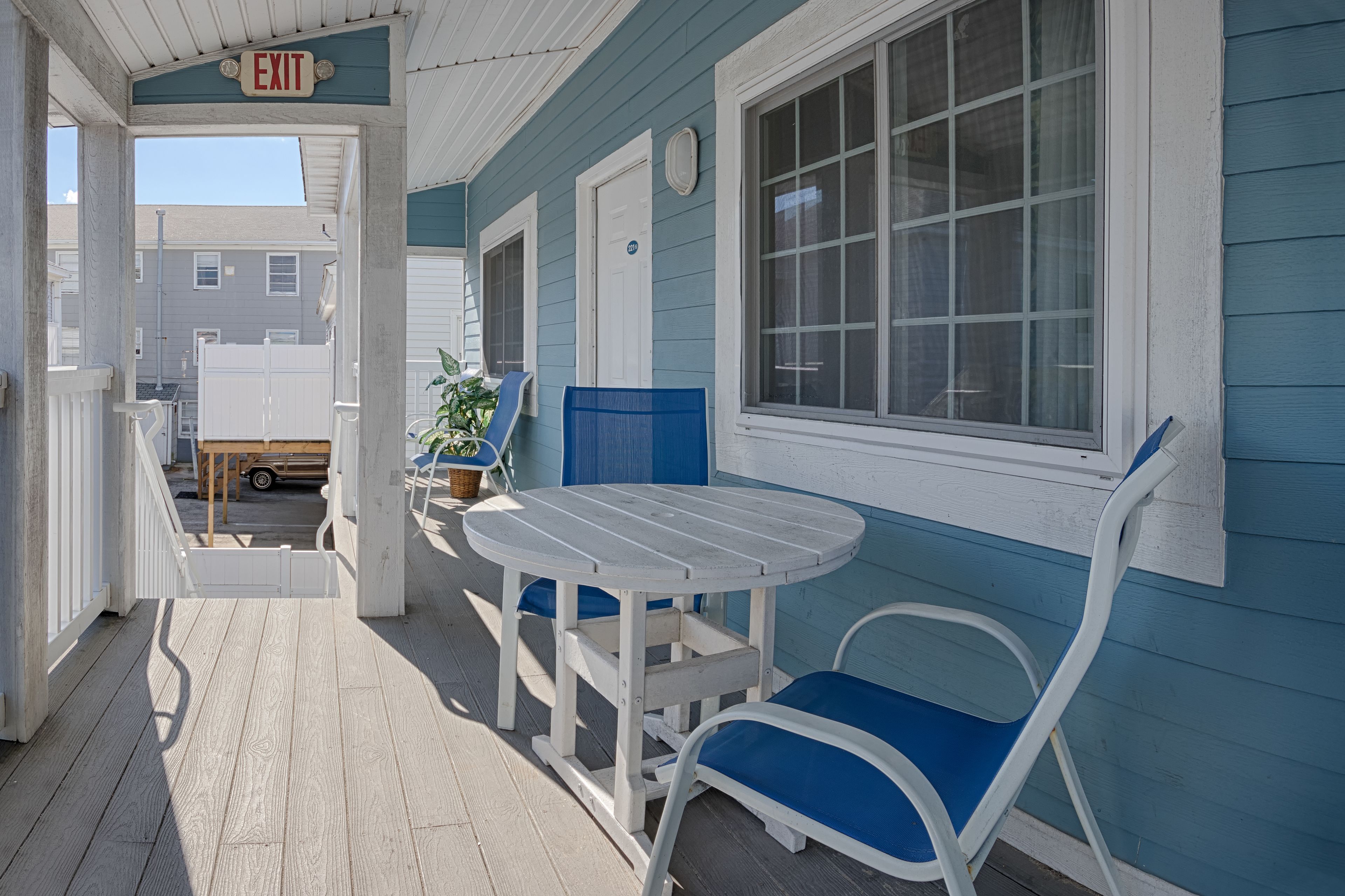 A covered porch with a table and chairs, an exit sign, and a view of the street.