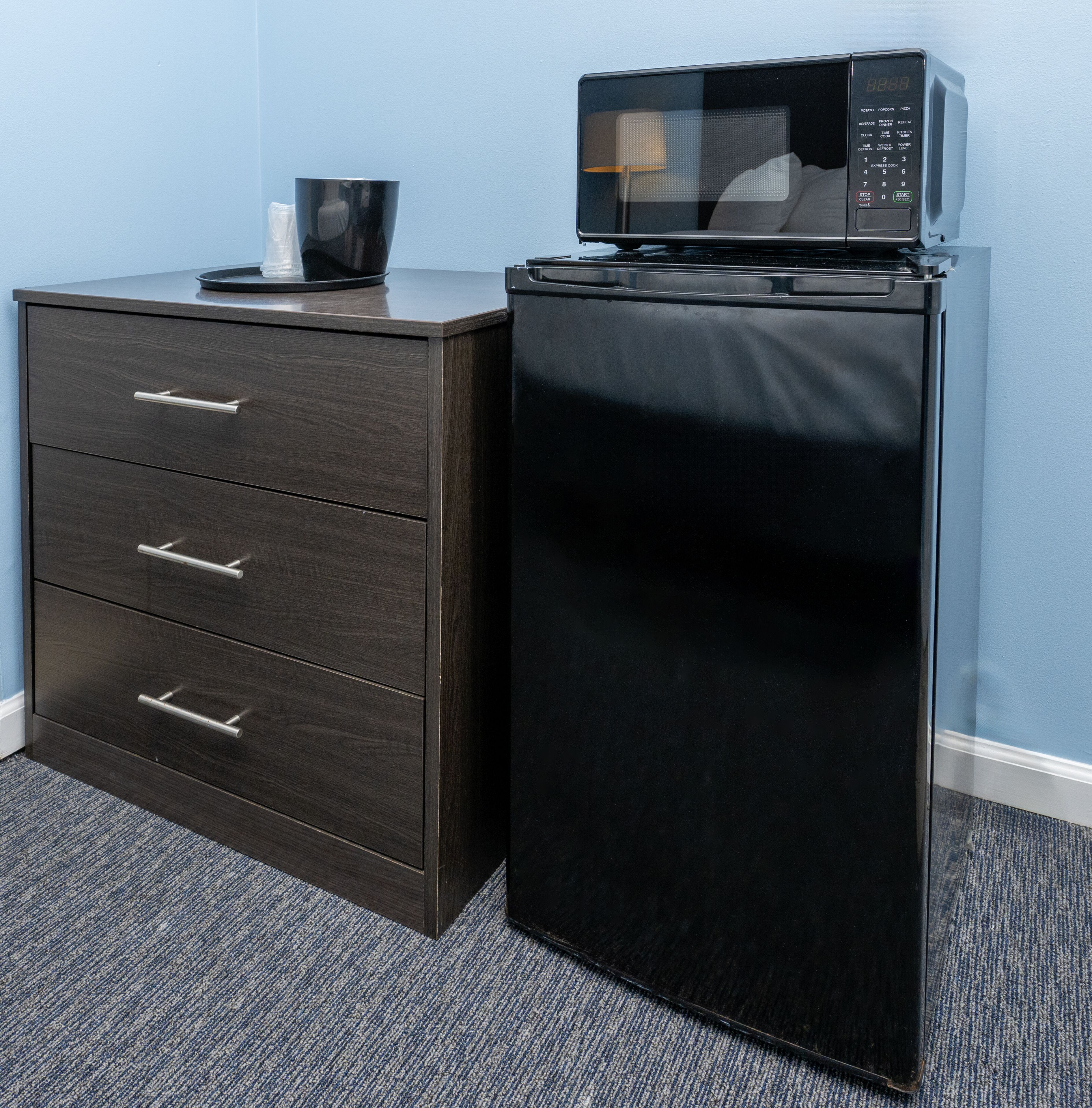 A compact kitchenette with a microwave and a dark wooden cabinet with drawers.