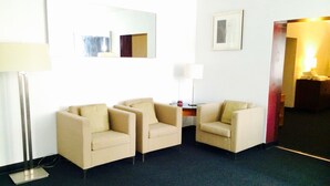 A hotel room with two beige armchairs, a small table with a lamp, a framed picture on the wall, and a mirror. - Stardust Motel and Suites El Dorado KS (El Dorado)