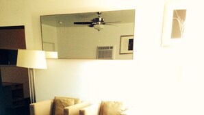 A living room with a sofa, armchairs, and a coffee table. There is a ceiling fan, a lamp, and a mirror on the wall. - Stardust Motel and Suites El Dorado KS (El Dorado)