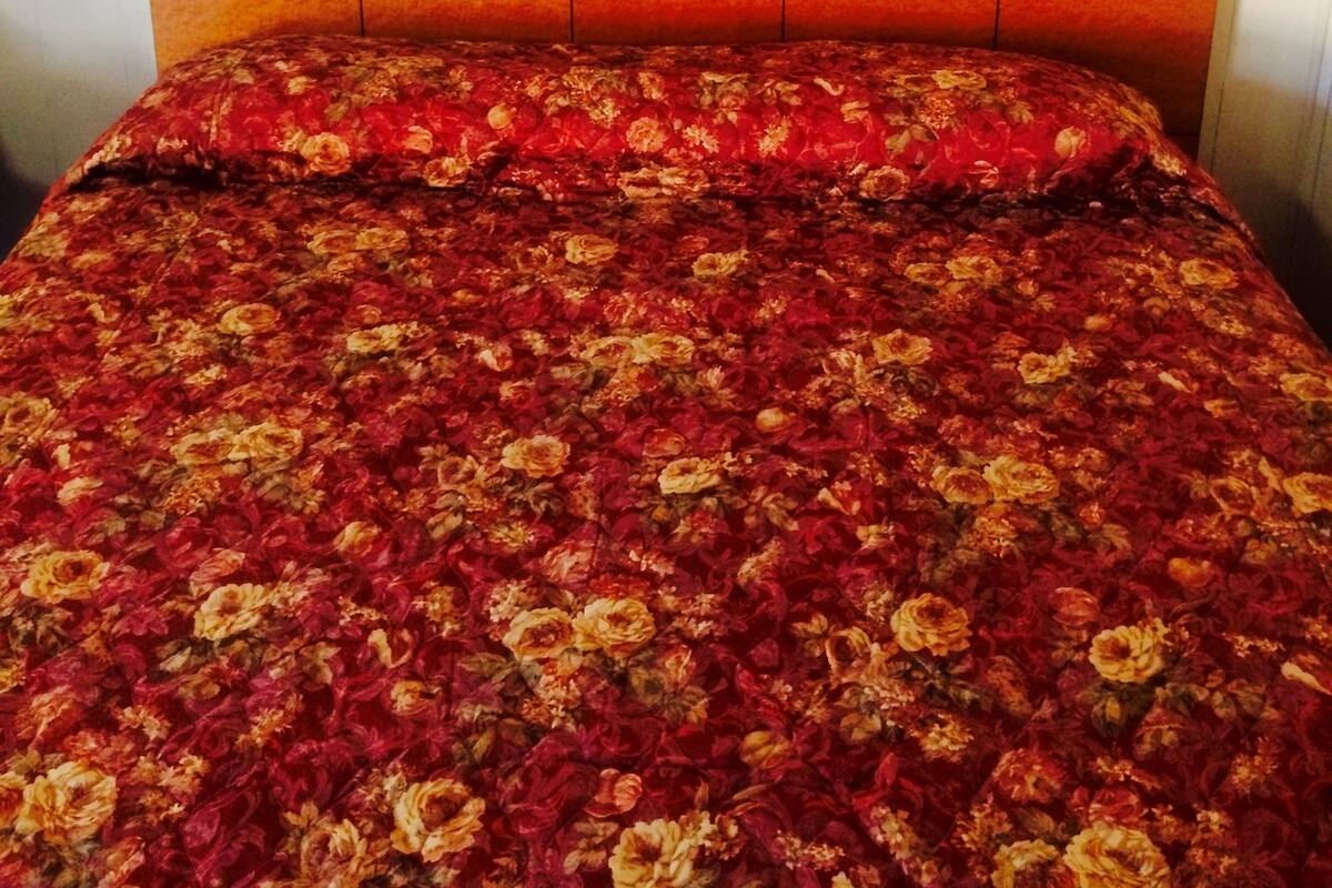 Un lit avec une couvre-lit à motifs floraux, une tête de lit au design incurvé et un tableau encadré accroché au mur.