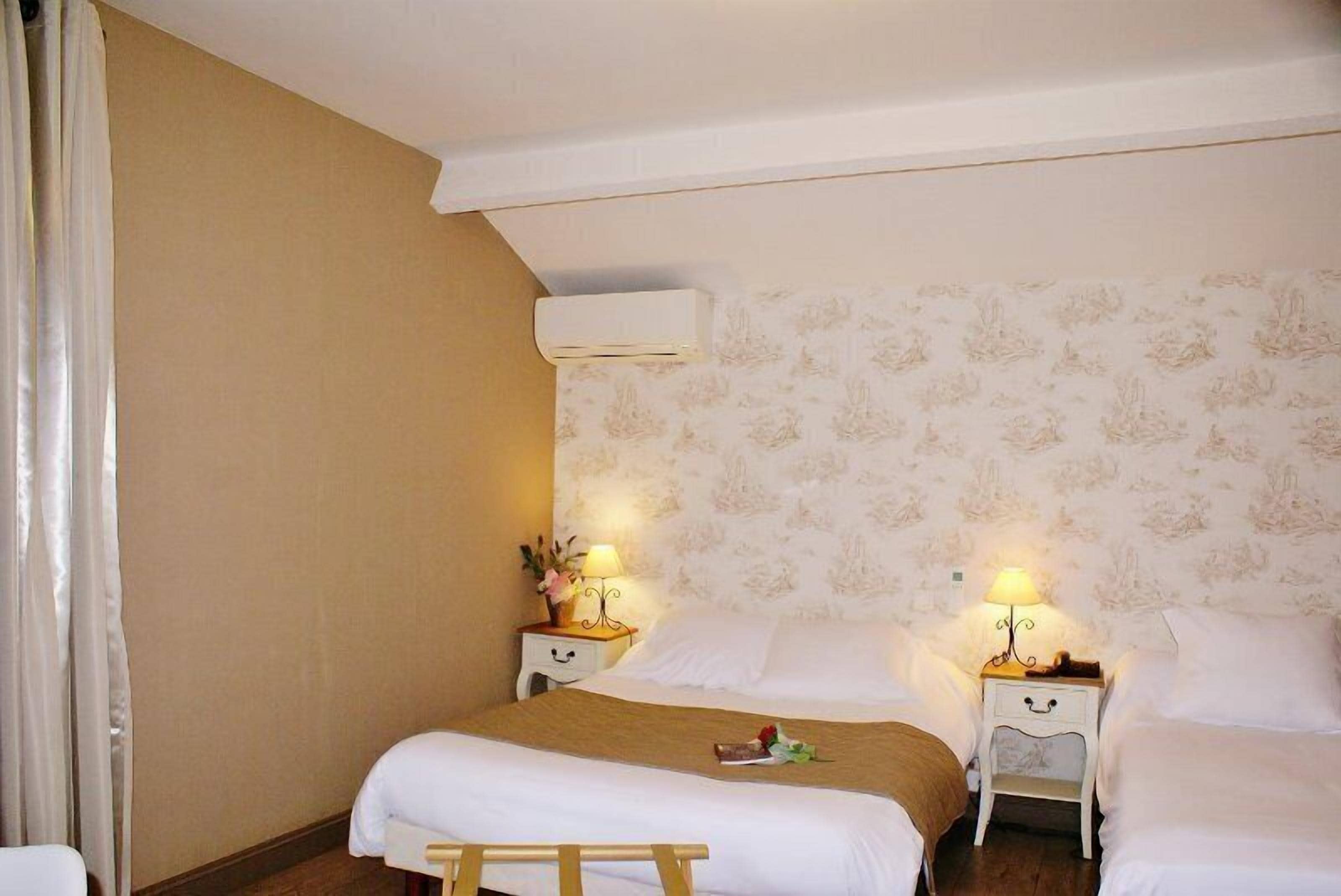 Een hotelkamer met twee bedden, een houten bankje en twee nachtkastjes met lampen.