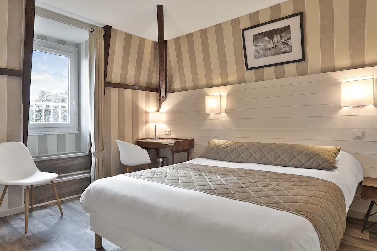 Una habitación de hotel con cama, escritorio, silla y ventana con cortinas.
