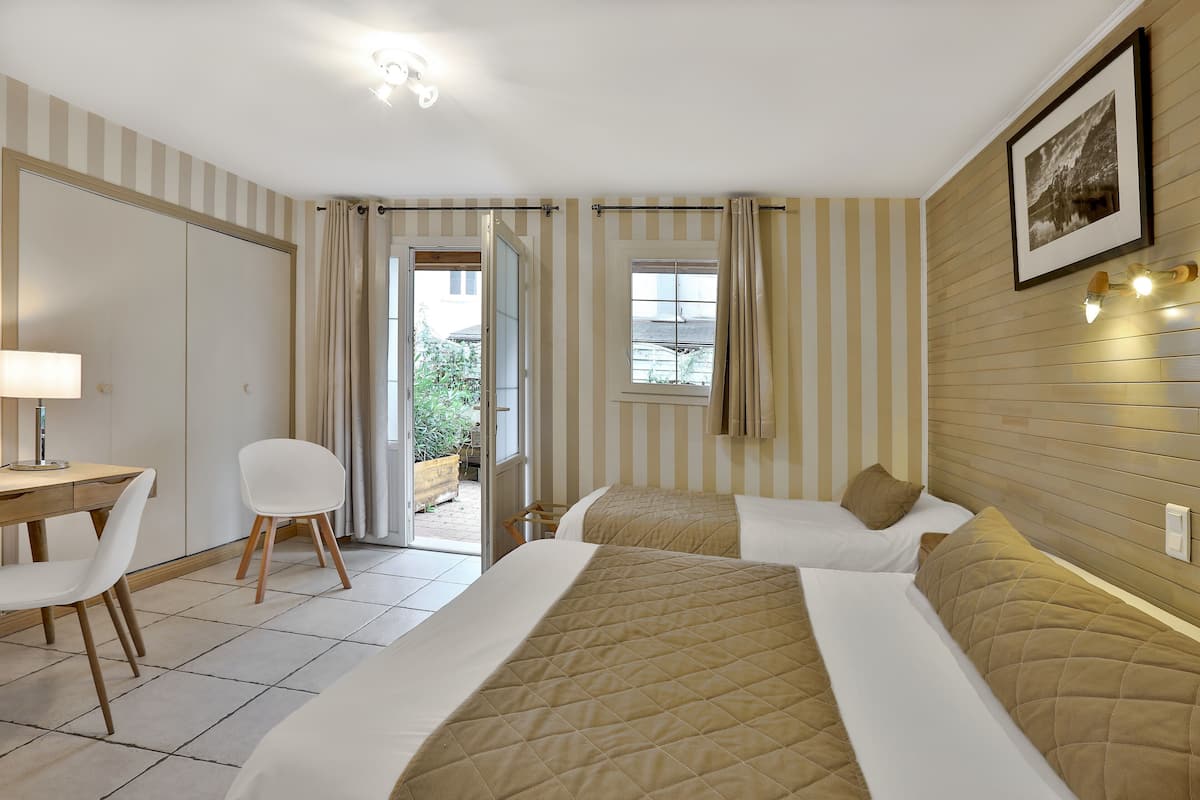Habitación de hotel con dos camas, un escritorio con silla, una ventana con cortinas y un cuadro en la pared.