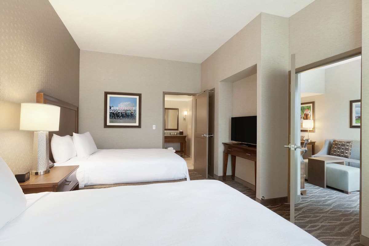 Ein Hotelzimmer mit zwei Betten, einem Fernseher, einem Schreibtisch und einer kleinen Sitzecke.