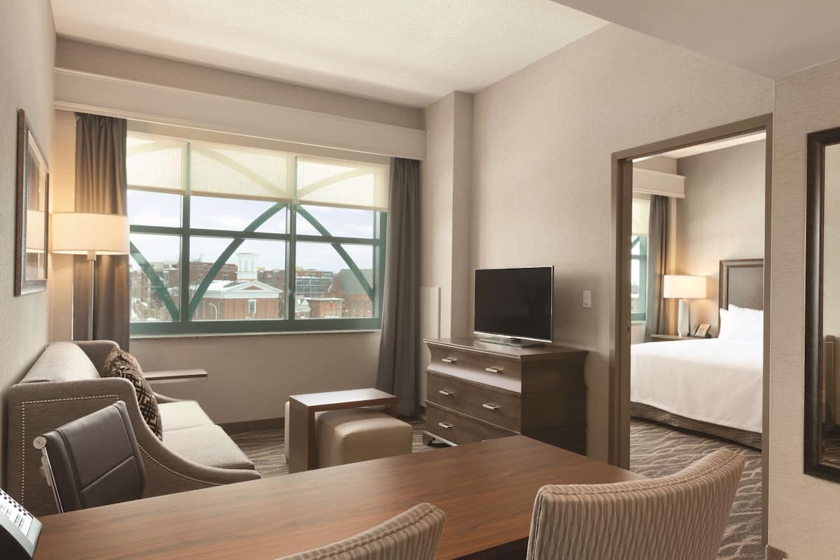 Ein Hotelzimmer mit großem Fenster, einem Bett, einem Schreibtisch, einem Fernseher und einer Sitzecke.