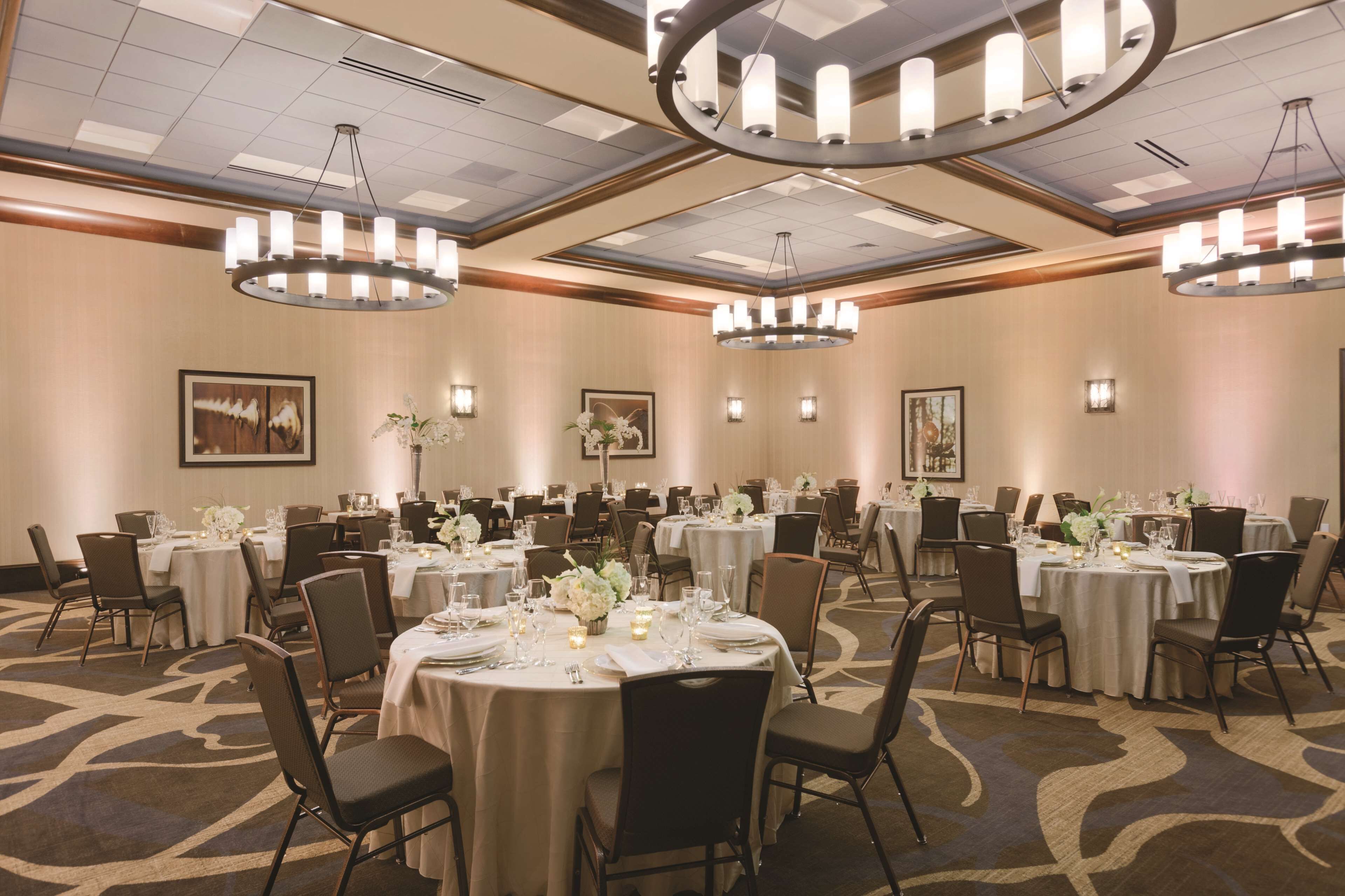 Une salle de banquet avec des tables rondes, des chaises, des lustres et des œuvres d’art encadrées accrochées aux murs.