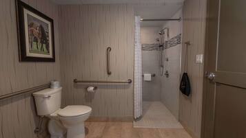 Un bany amb vàter, dutxa amb barana de suport, quadre encapçalat a la paret i paraigua de tovalloles.