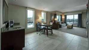Une chambre d’hôtel avec un coin repas, une grande fenêtre donnant sur la ville, un canapé et une petite table.