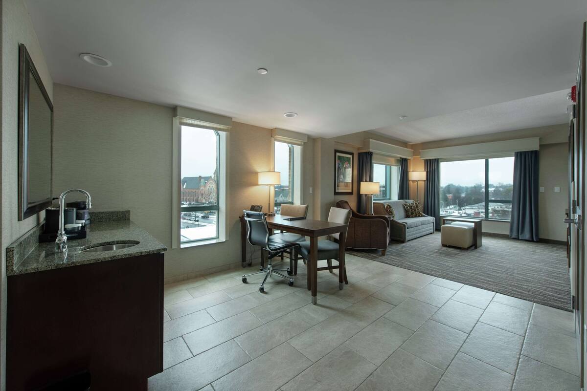 Ein Hotelzimmer mit Essbereich, einem großen Fenster mit Blick auf die Stadt, einer Couch und einem kleinen Tisch.