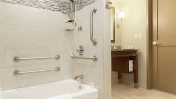 A modern bathroom with a bathtub, grab bars, a shower with a handheld showerhead, and a vanity with a towel rack.
