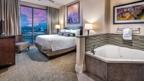 Habitación de hotel con una cama grande, zona de estar, bañera y vista a la ciudad.