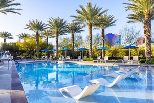 A swimming pool with lounge chairs and umbrellas, surrounded by palm trees and a clear sky.