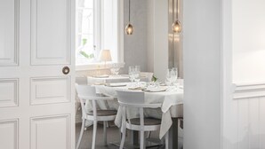 A dining area with white tables and chairs, a window with a view, and pendant lights. - Hotel Villa Anna (Uppsala)
